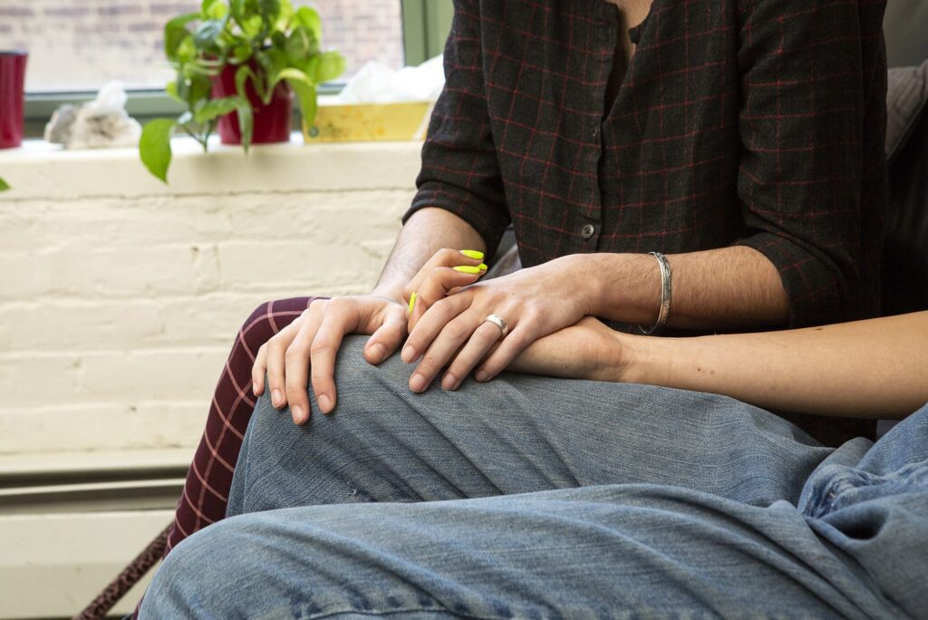 A parent and their trans son holding hands on a couch
